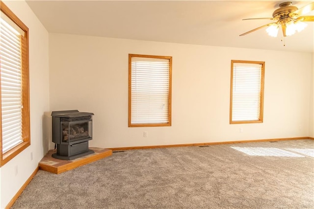 unfurnished living room featuring carpet floors, a wood stove, and ceiling fan