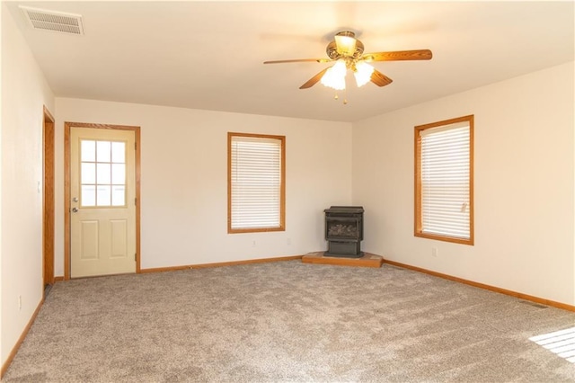 carpeted empty room featuring ceiling fan and a wood stove