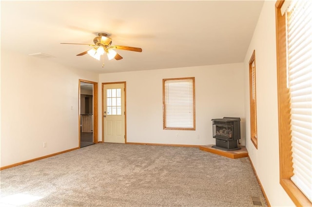 unfurnished living room featuring carpet floors, ceiling fan, and a wood stove