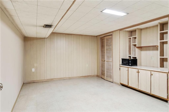 spare room featuring light floors, wood walls, visible vents, and baseboards