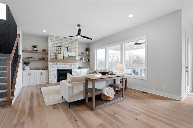 living room featuring ceiling fan, a brick fireplace, and light wood-type flooring