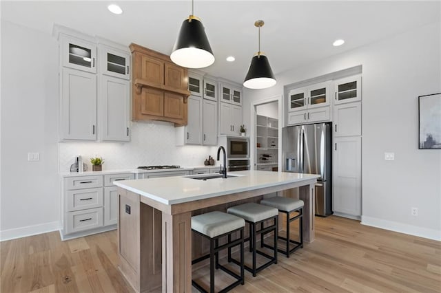 kitchen featuring appliances with stainless steel finishes, white cabinetry, an island with sink, sink, and hanging light fixtures