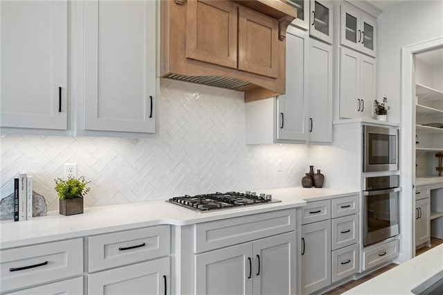 kitchen featuring tasteful backsplash, custom exhaust hood, stainless steel appliances, and white cabinets