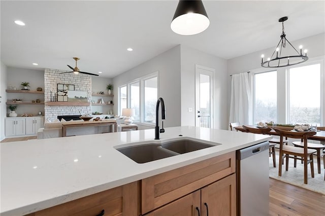 kitchen with dishwasher, sink, hanging light fixtures, a brick fireplace, and light wood-type flooring