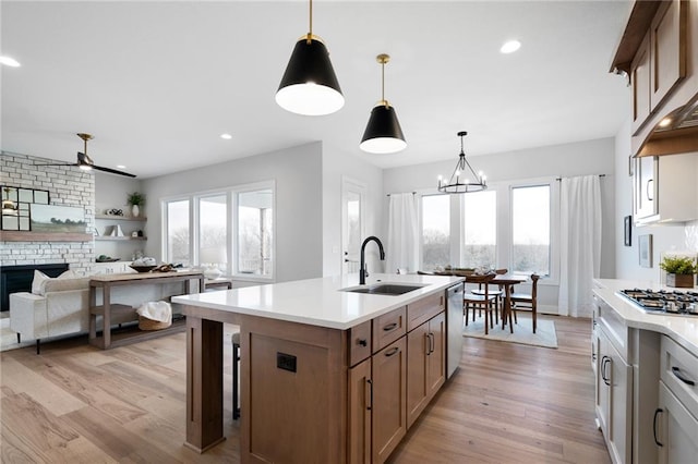 kitchen with appliances with stainless steel finishes, a fireplace, an island with sink, sink, and hanging light fixtures