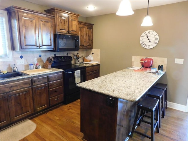 kitchen with pendant lighting, tasteful backsplash, a kitchen breakfast bar, hardwood / wood-style flooring, and black appliances