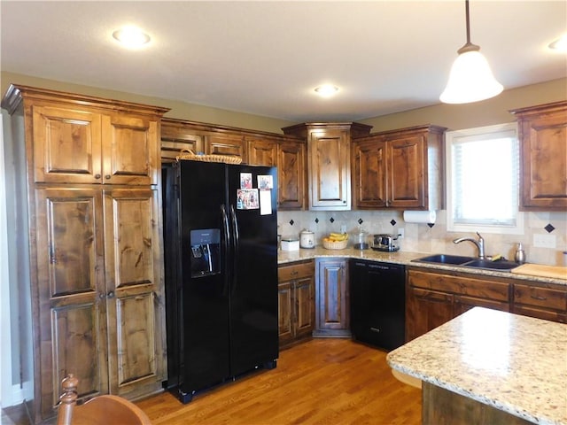 kitchen featuring sink, hanging light fixtures, light hardwood / wood-style flooring, decorative backsplash, and black appliances