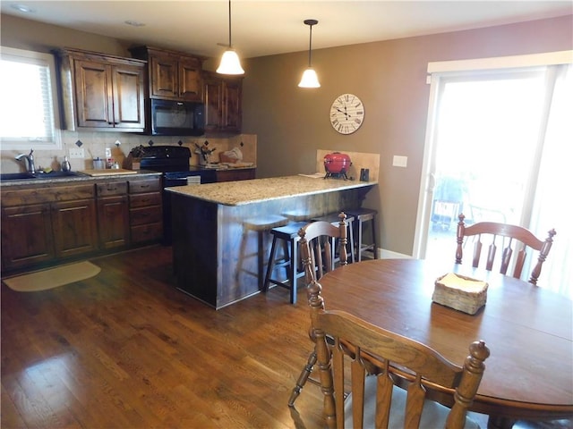 kitchen with pendant lighting, sink, a kitchen breakfast bar, decorative backsplash, and black appliances