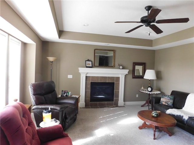 carpeted living room featuring ceiling fan, a fireplace, and a raised ceiling