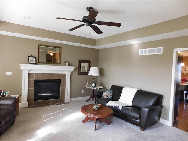 living room with a tile fireplace, ceiling fan, and carpet flooring