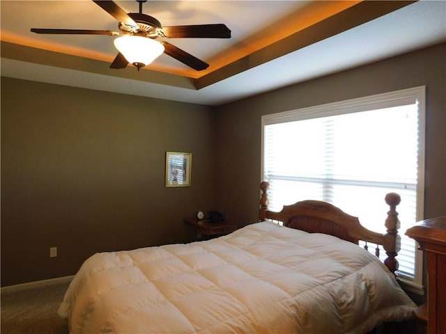 carpeted bedroom featuring a tray ceiling and ceiling fan