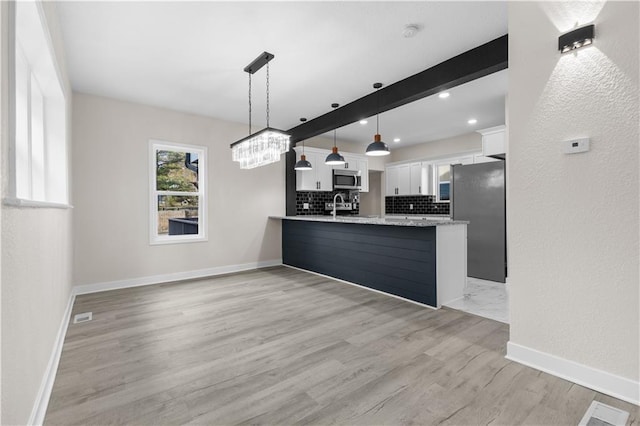 kitchen with decorative light fixtures, appliances with stainless steel finishes, kitchen peninsula, white cabinets, and backsplash