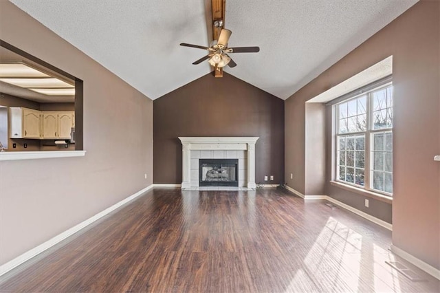 unfurnished living room with ceiling fan, hardwood / wood-style floors, vaulted ceiling with beams, a textured ceiling, and a tiled fireplace