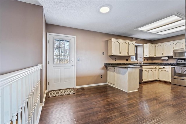 kitchen with sink, appliances with stainless steel finishes, dark hardwood / wood-style floors, a textured ceiling, and kitchen peninsula