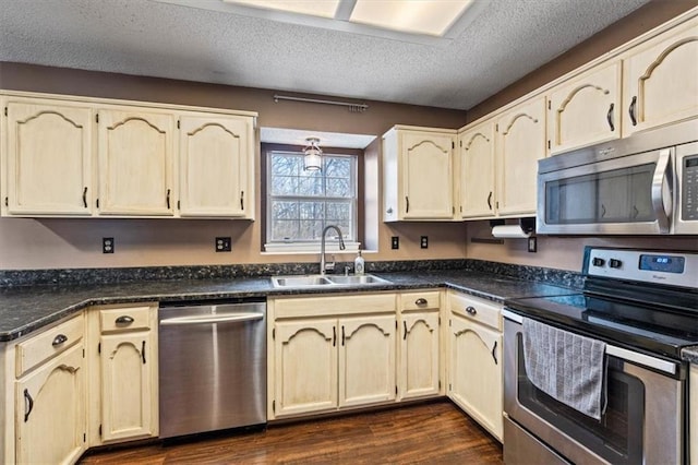 kitchen with appliances with stainless steel finishes, sink, cream cabinets, dark wood-type flooring, and a textured ceiling