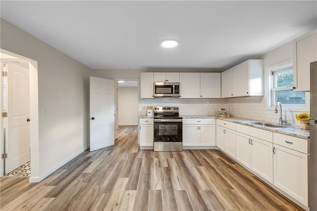 kitchen with white cabinets, appliances with stainless steel finishes, a sink, and light wood-style flooring