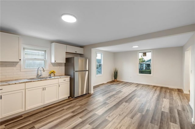 kitchen with freestanding refrigerator, light stone countertops, tasteful backsplash, a sink, and light wood finished floors
