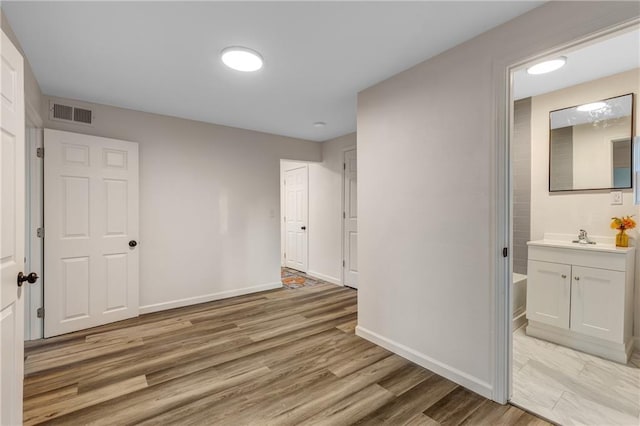 unfurnished bedroom featuring visible vents, a sink, baseboards, and light wood finished floors