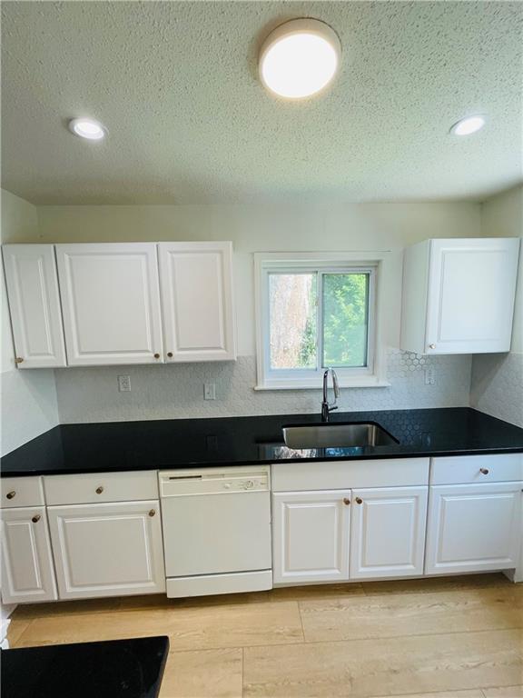 kitchen featuring white cabinetry, dishwasher, sink, and a textured ceiling