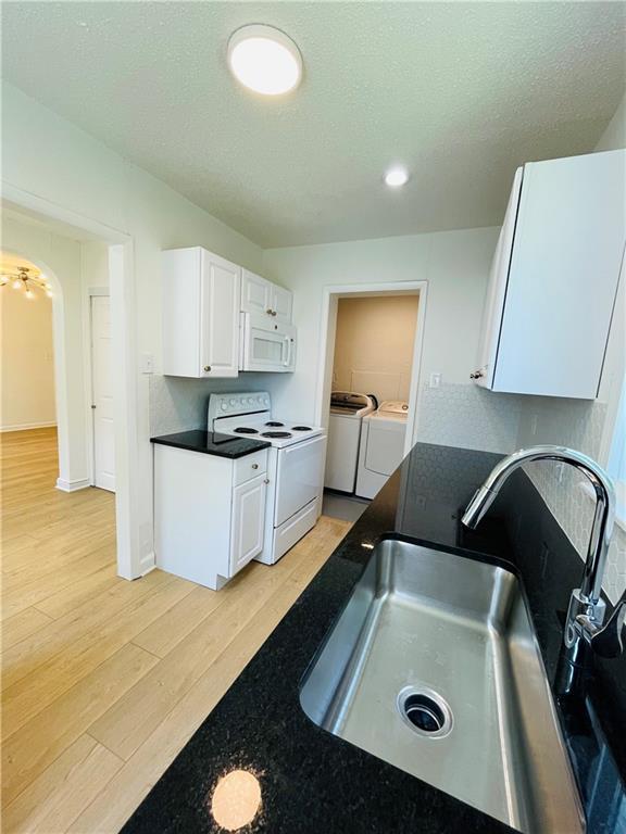 kitchen featuring sink, light wood-type flooring, white cabinets, independent washer and dryer, and white appliances