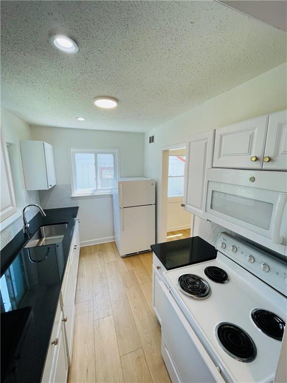 kitchen featuring sink, white cabinetry, a textured ceiling, white appliances, and light hardwood / wood-style floors