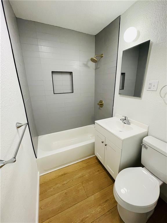 full bathroom with wood-type flooring, tiled shower / bath, vanity, and toilet