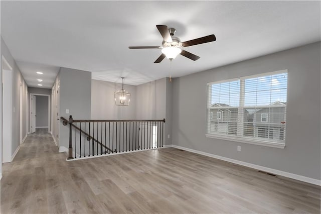 empty room with ceiling fan with notable chandelier and light hardwood / wood-style floors