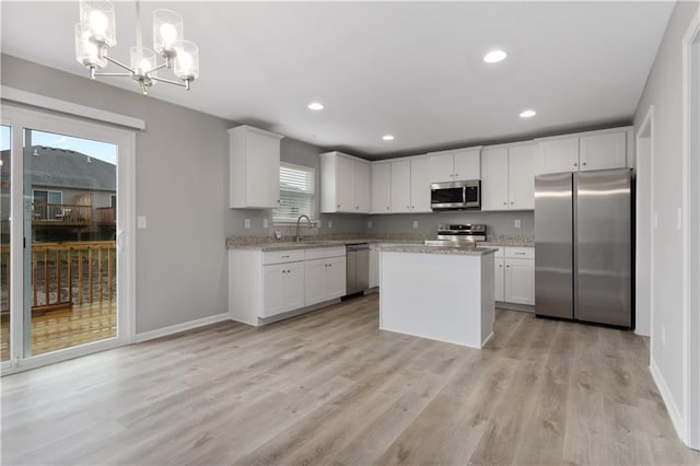 kitchen with a center island, decorative light fixtures, appliances with stainless steel finishes, white cabinetry, and a sink