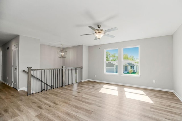 empty room with light wood finished floors, baseboards, and ceiling fan with notable chandelier