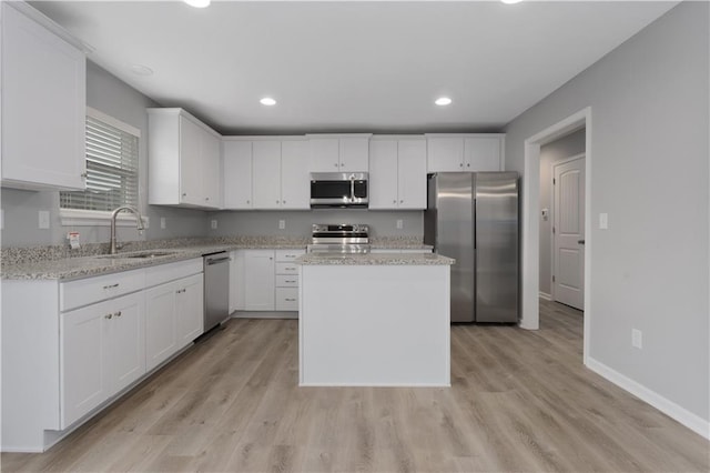 kitchen with a kitchen island, light stone counters, stainless steel appliances, white cabinetry, and a sink