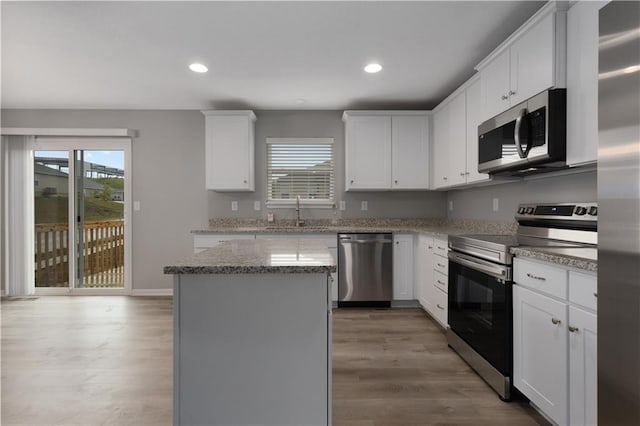 kitchen with appliances with stainless steel finishes, light stone counters, a center island, white cabinetry, and a sink