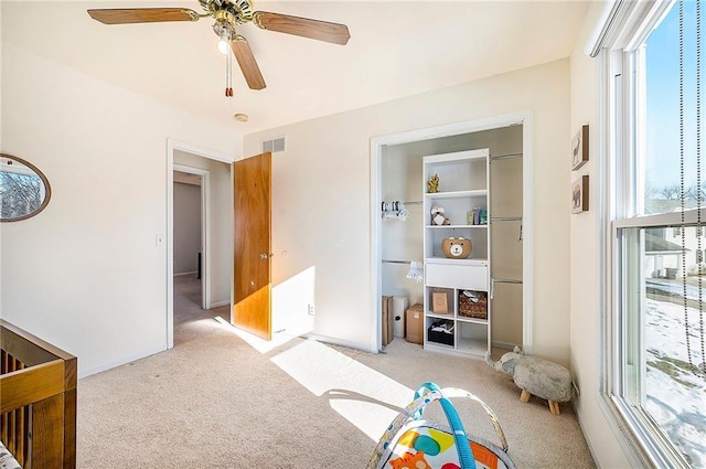 bedroom featuring light carpet, a nursery area, and ceiling fan