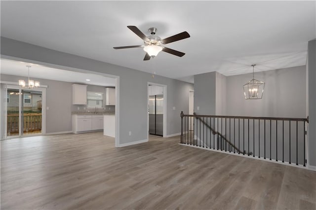 unfurnished living room featuring sink, ceiling fan with notable chandelier, and light hardwood / wood-style flooring