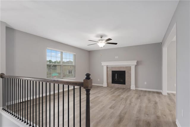 unfurnished living room featuring ceiling fan, a tile fireplace, and light wood-type flooring