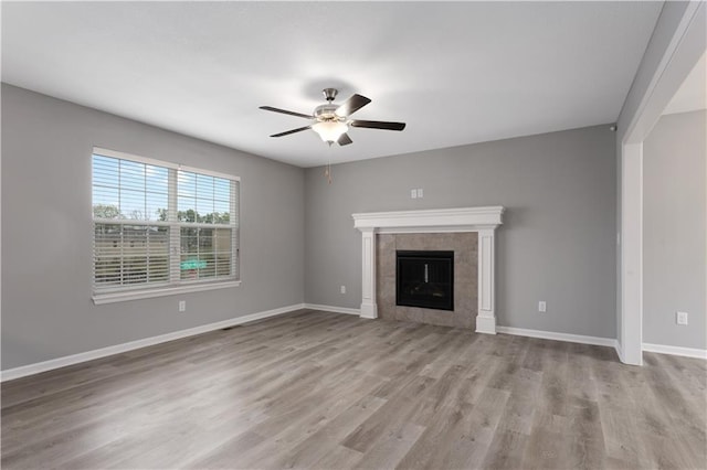 unfurnished living room featuring a tiled fireplace, ceiling fan, and light wood-type flooring