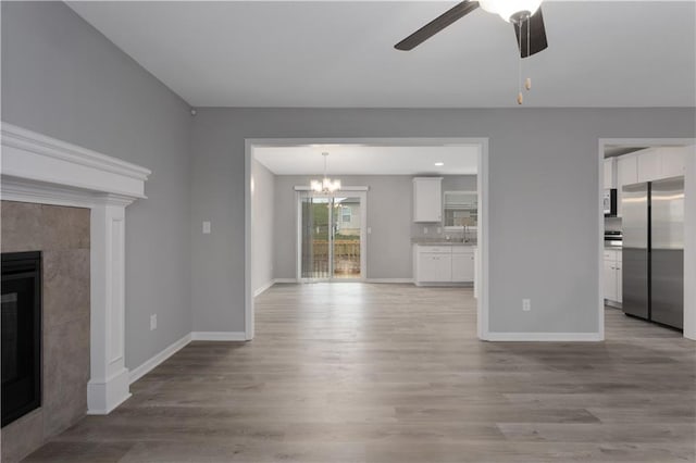 unfurnished living room featuring a tiled fireplace, ceiling fan with notable chandelier, and light wood-type flooring