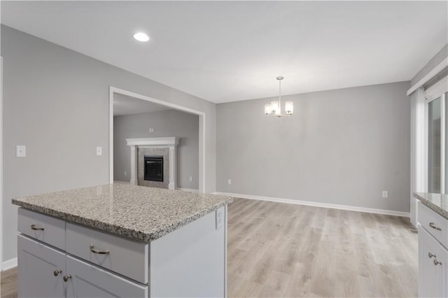 kitchen featuring a kitchen island, pendant lighting, a chandelier, light stone counters, and light hardwood / wood-style floors