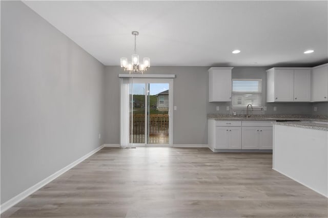 kitchen featuring white cabinetry, sink, light wood-type flooring, hanging light fixtures, and an inviting chandelier