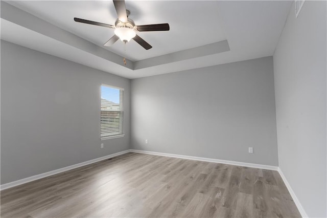 empty room with a tray ceiling, ceiling fan, and light wood-type flooring