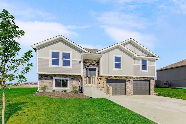 bi-level home with board and batten siding, a front yard, stone siding, and concrete driveway