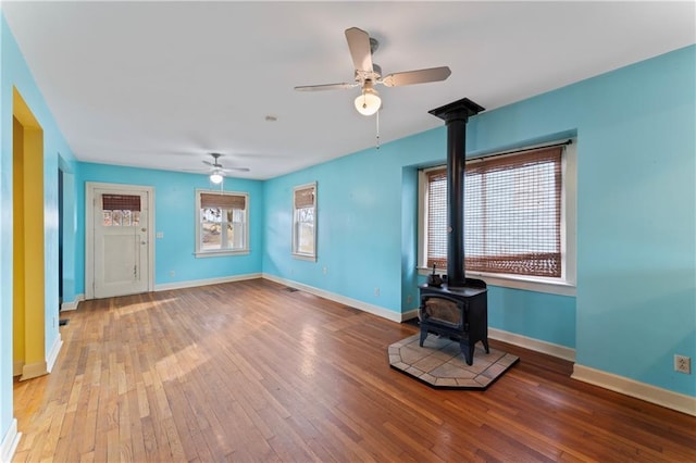 unfurnished living room with hardwood / wood-style flooring, ceiling fan, and a wood stove