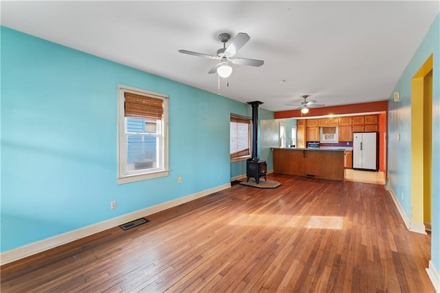 unfurnished living room with ceiling fan, a wood stove, and light hardwood / wood-style floors