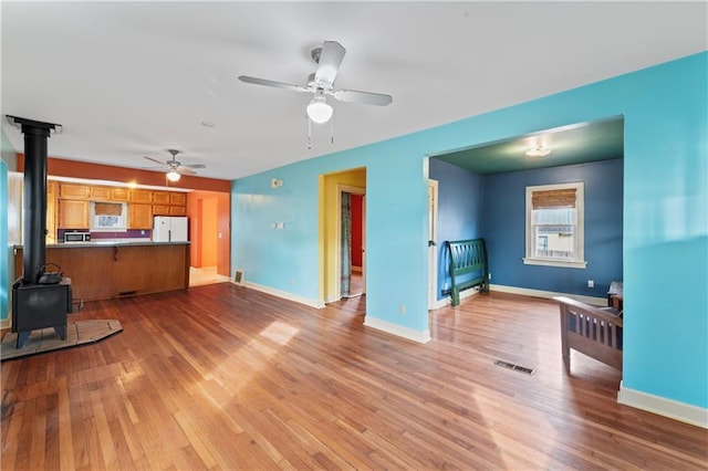 unfurnished living room with ceiling fan, a wood stove, and light hardwood / wood-style floors