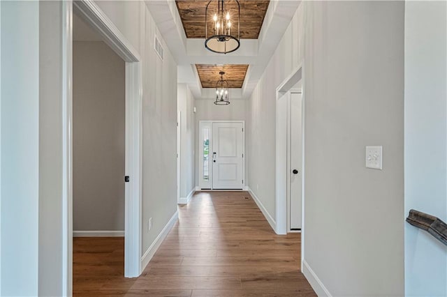 hallway featuring an inviting chandelier, hardwood / wood-style floors, a tray ceiling, and wooden ceiling