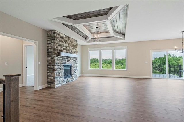 unfurnished living room featuring plenty of natural light, a stone fireplace, a chandelier, and wood-type flooring