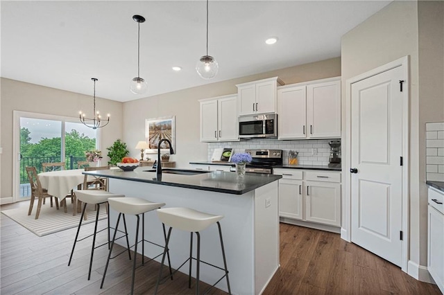 kitchen with a sink, white cabinets, appliances with stainless steel finishes, dark countertops, and a center island with sink