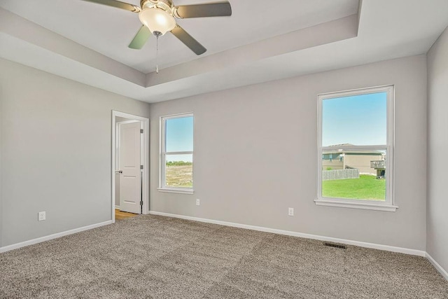 carpeted empty room featuring a tray ceiling, a ceiling fan, visible vents, and baseboards