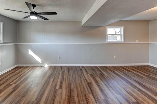 unfurnished room with ceiling fan, dark wood-type flooring, a textured ceiling, and wooden walls