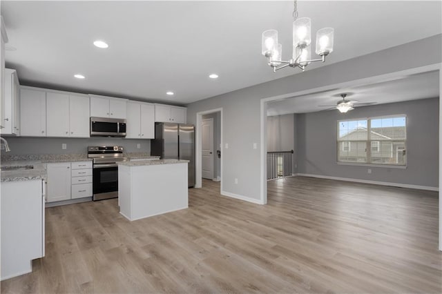 kitchen featuring stainless steel appliances, a kitchen island, white cabinetry, open floor plan, and decorative light fixtures