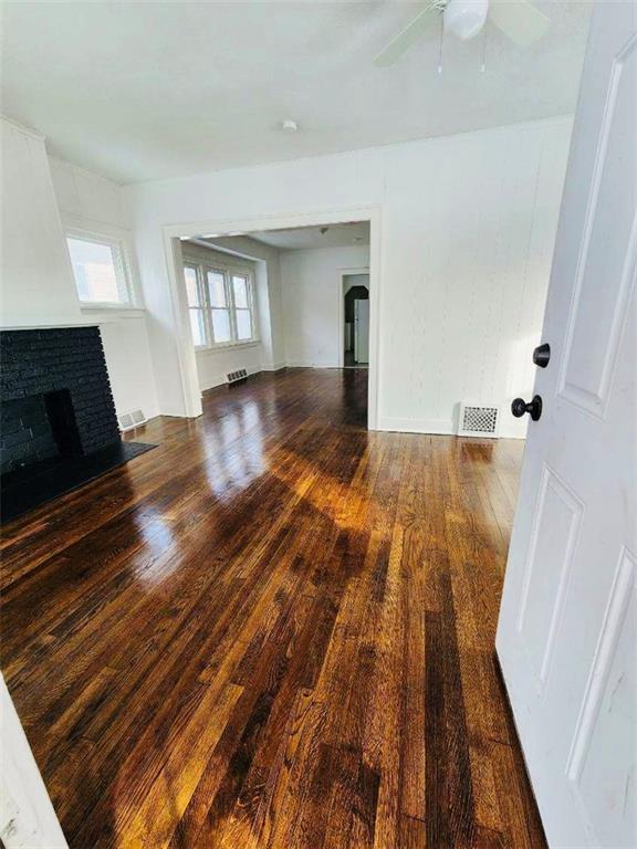 unfurnished living room featuring a brick fireplace, dark wood-type flooring, and ceiling fan